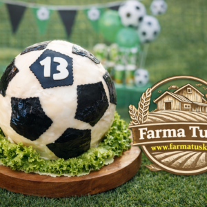 Syrová torta v tvare futbalovej lopty s číslom 13 na drevenom podnose so zeleným šalátom, na detskej futbalovej oslave s logom Farma Tuška a zvýraznenou webovou adresou www.farmatuska.sk .